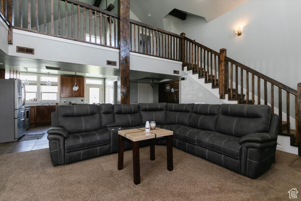 Living area with a towering ceiling, stairway, and light carpet