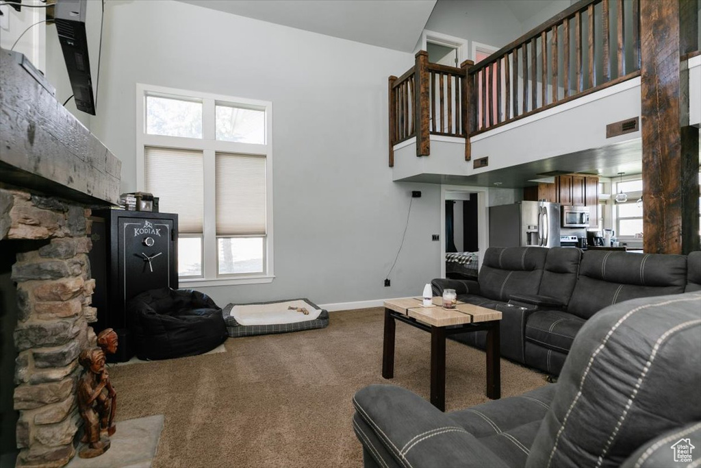 Living room featuring a towering ceiling, carpet flooring, a fireplace, healthy amount of natural light, and baseboards