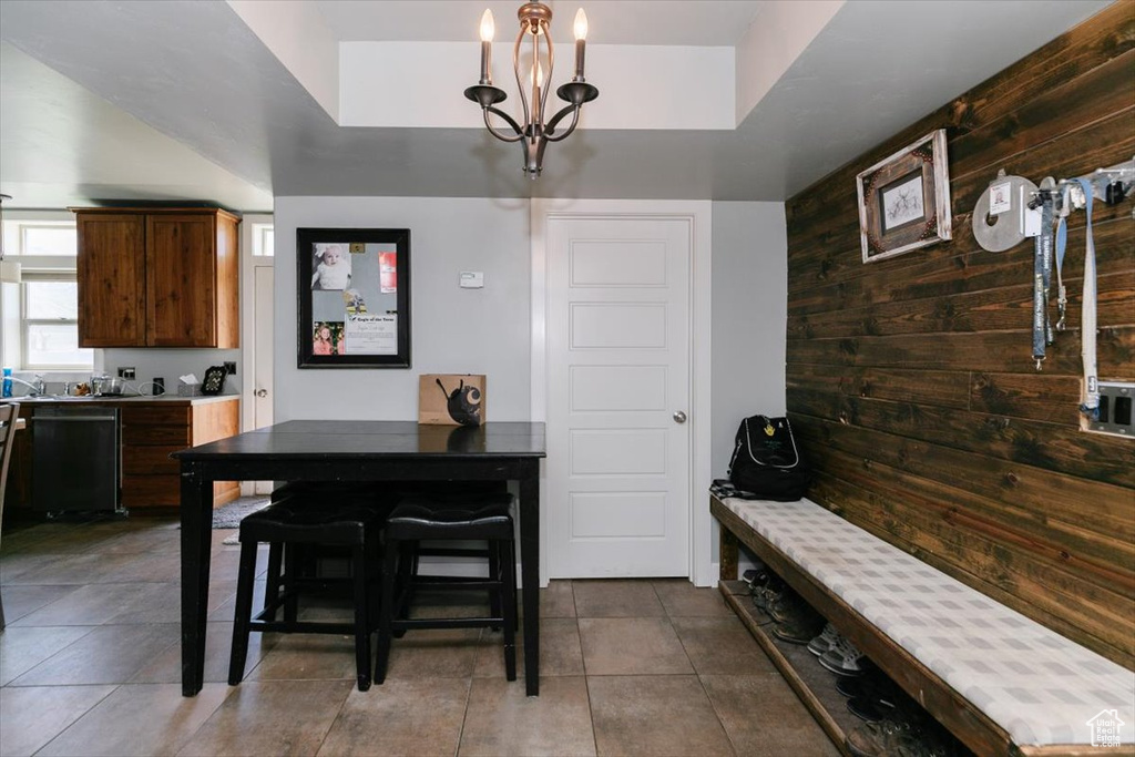 Dining space with dark tile patterned flooring, wood walls, and a notable chandelier