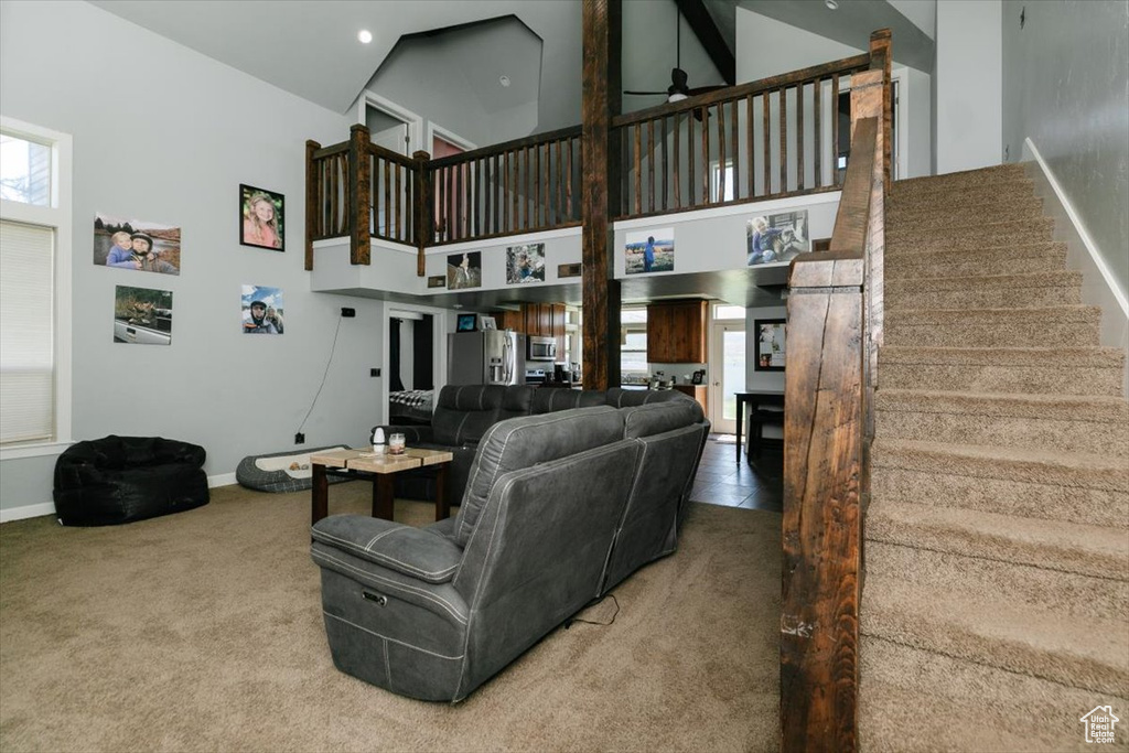 Living room featuring ceiling fan, baseboards, a high ceiling, carpet flooring, and stairs
