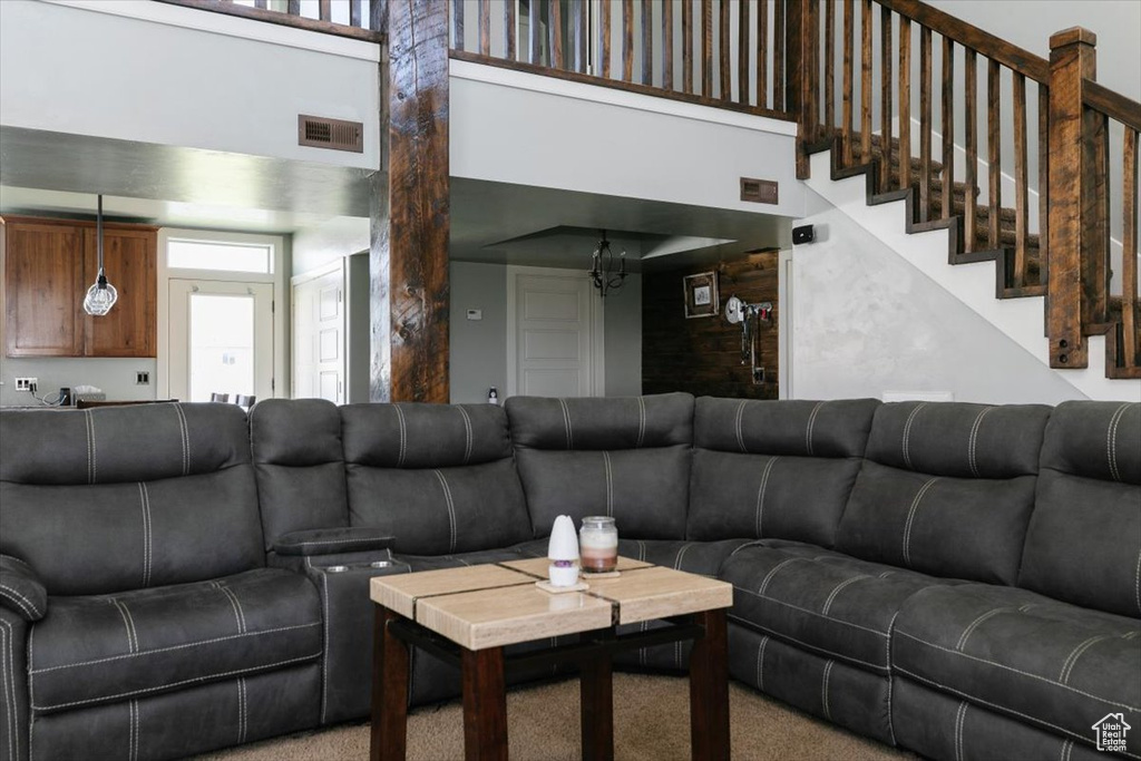 Living room with a high ceiling, healthy amount of natural light, carpet flooring, and a chandelier