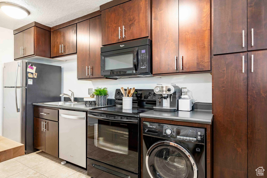Kitchen with dark brown cabinets, a sink, black appliances, light tile patterned floors, and washer / dryer
