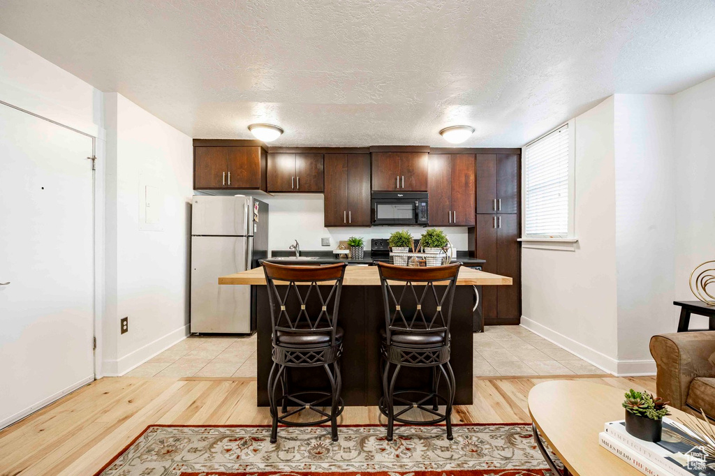 Kitchen with black microwave, dark brown cabinets, light wood-style floors, and freestanding refrigerator