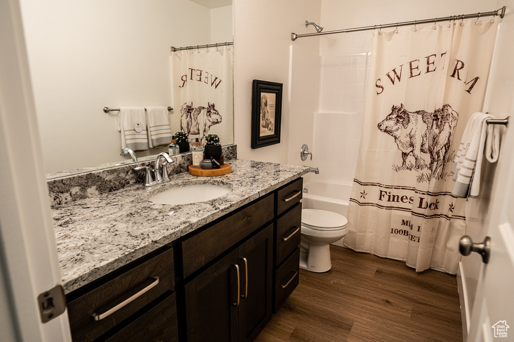 Bathroom with wood finished floors, toilet, vanity, and shower / bath combination with curtain