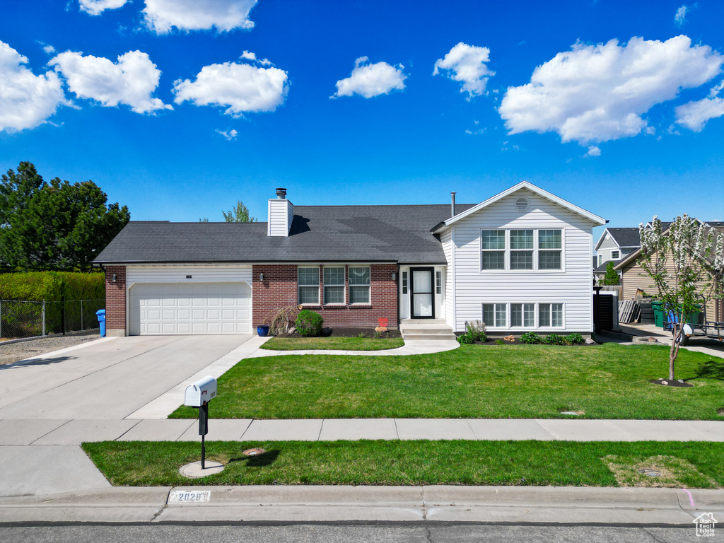 Tri-level home featuring an attached garage, brick siding, a front yard, a chimney, and concrete driveway