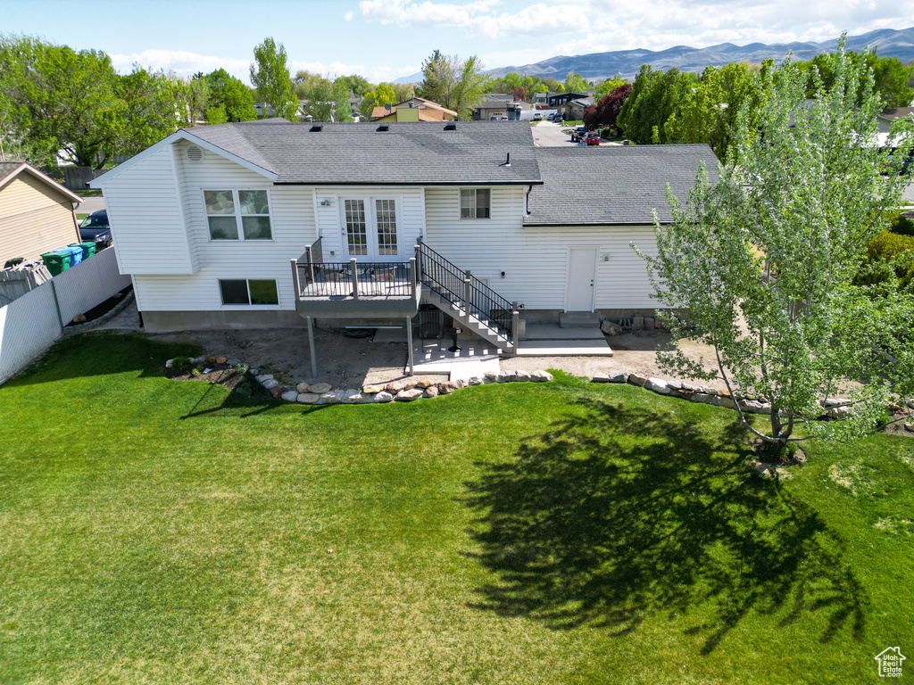 Back of property featuring fence, stairs, a shingled roof, a deck with mountain view, and a lawn