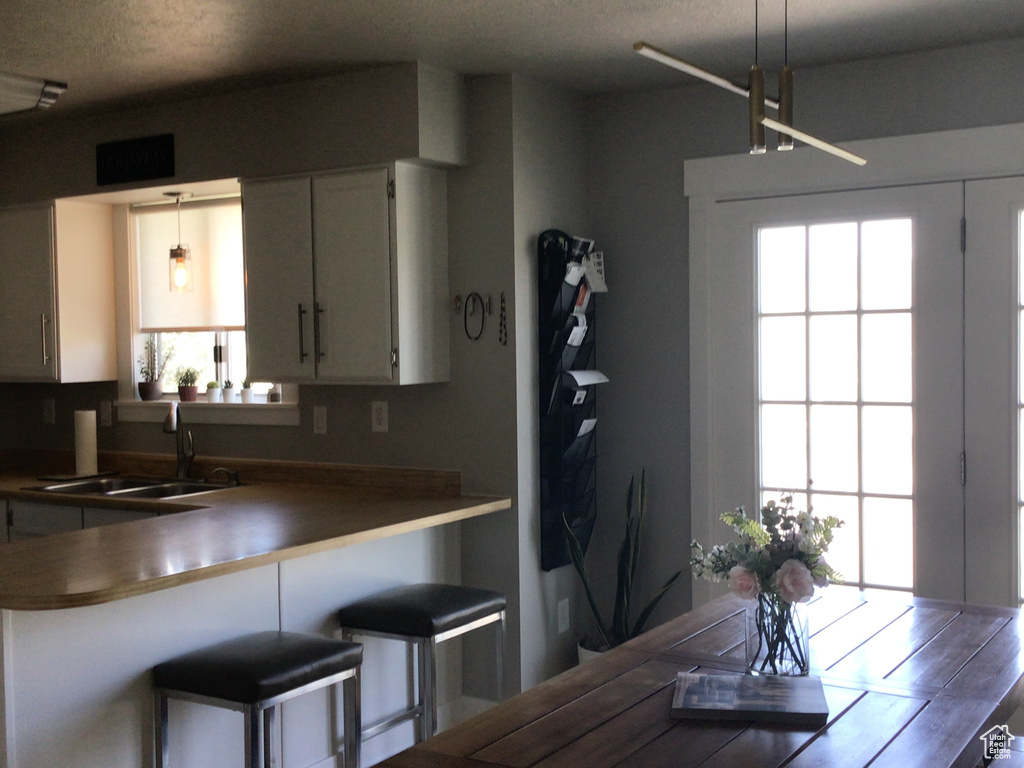 Kitchen featuring white cabinets, hanging light fixtures, a sink, and a textured ceiling