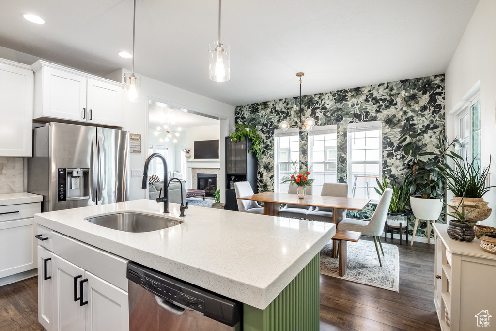 Kitchen with a sink, an island with sink, a glass covered fireplace, an inviting chandelier, and stainless steel appliances