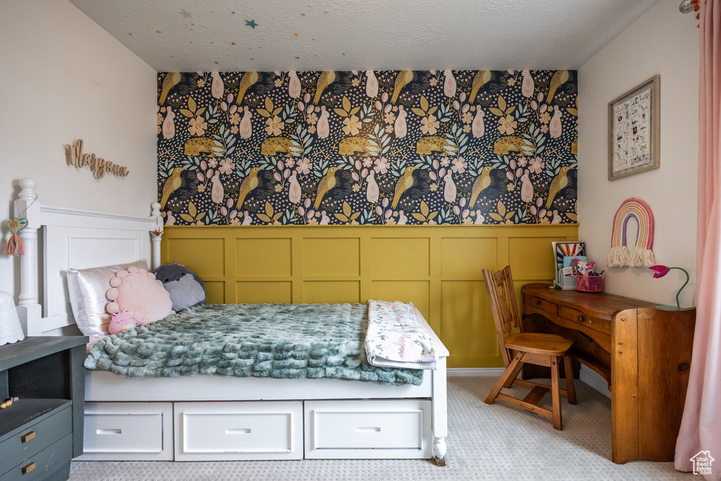 Bedroom featuring light colored carpet, a decorative wall, a wainscoted wall, and wallpapered walls