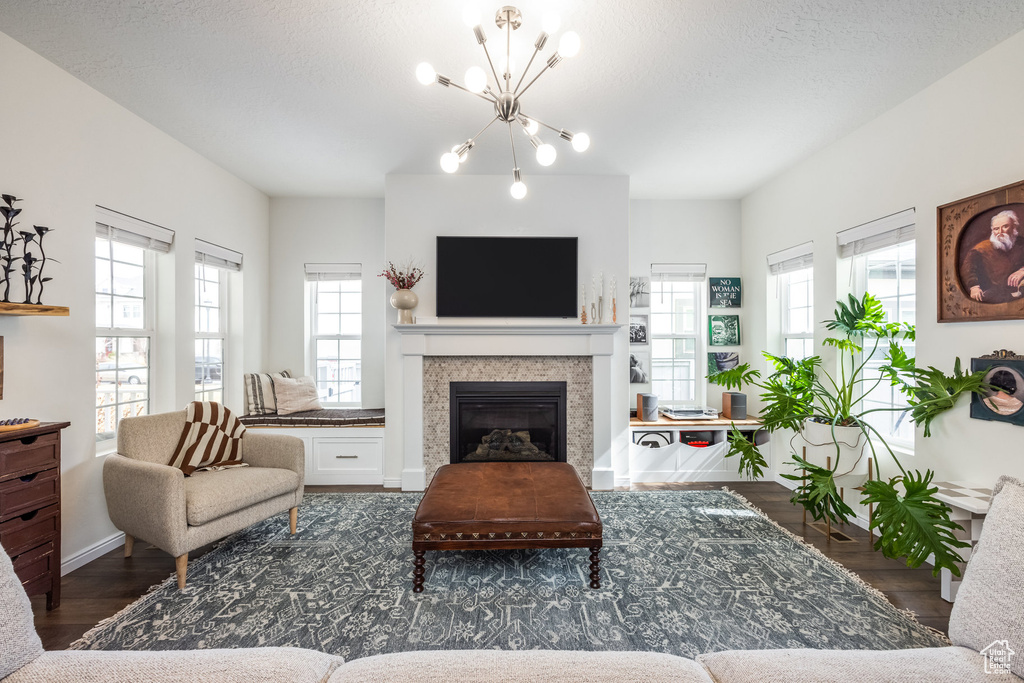 Living area featuring a textured ceiling, baseboards, a glass covered fireplace, an inviting chandelier, and wood finished floors