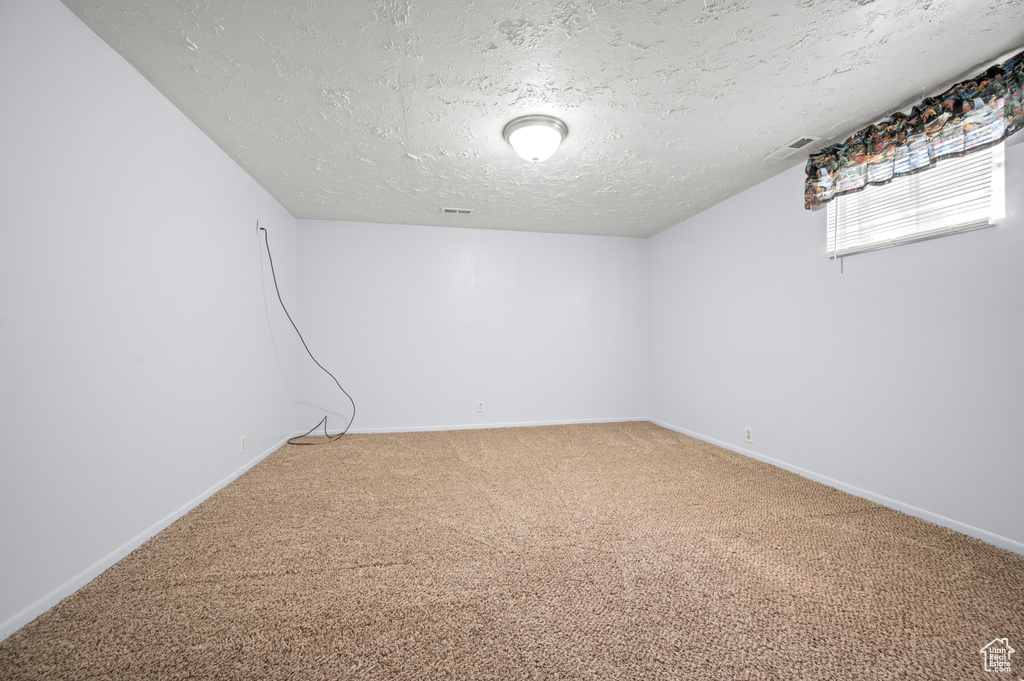 Below grade area with a textured ceiling, visible vents, light carpet, and baseboards