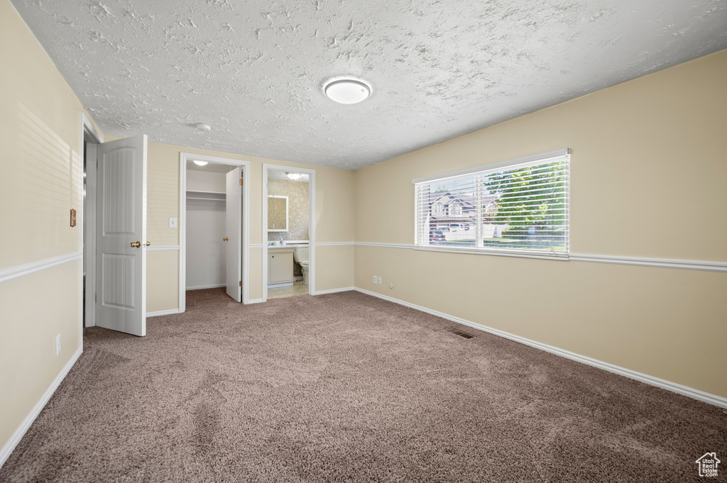 Unfurnished bedroom with baseboards, carpet flooring, a textured ceiling, and a walk in closet