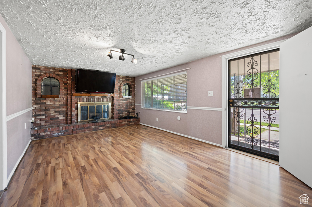 Unfurnished living room with a brick fireplace, a textured ceiling, baseboards, and wood finished floors