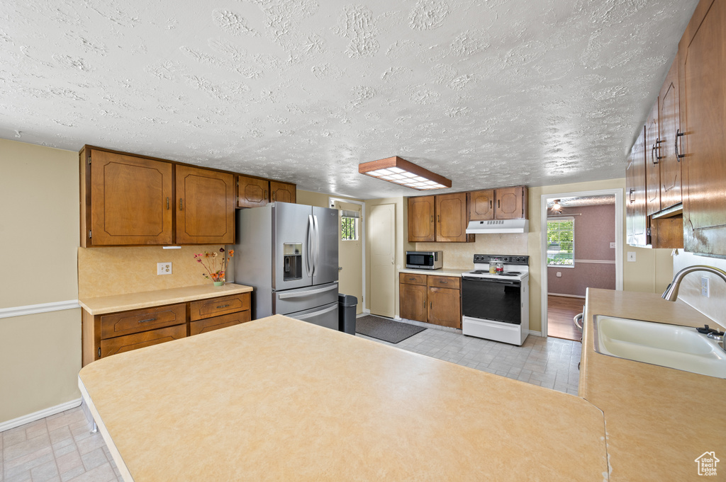 Kitchen with brown cabinets, a sink, baseboards, under cabinet range hood, and stainless steel appliances