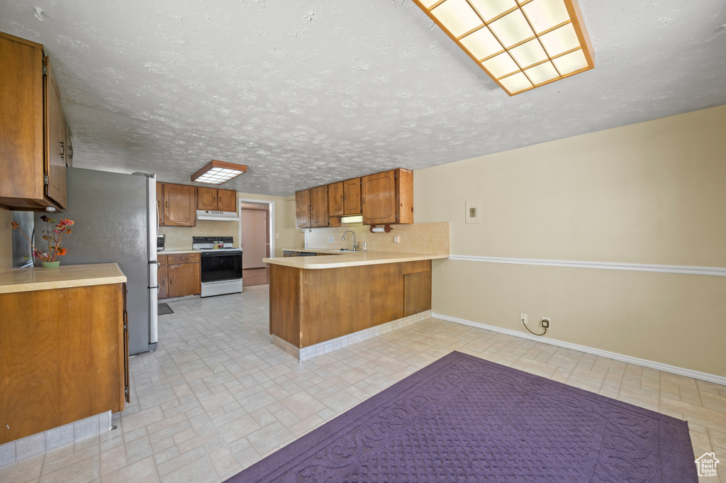 Kitchen featuring light countertops, range with electric cooktop, brown cabinetry, a peninsula, and under cabinet range hood