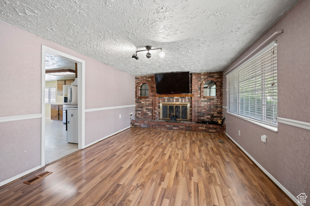 Unfurnished living room with a textured ceiling, a brick fireplace, wood finished floors, and visible vents