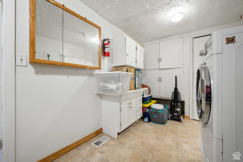 Clothes washing area with cabinet space, a textured ceiling, baseboards, washer / dryer, and visible vents