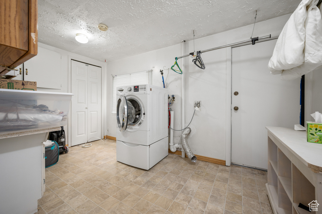 Washroom with baseboards, washer / clothes dryer, stone finish floor, a textured ceiling, and cabinet space