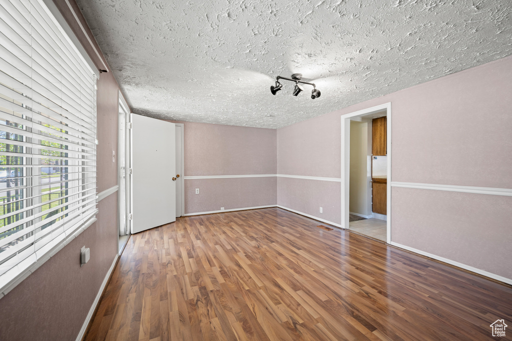 Empty room featuring a textured ceiling, baseboards, and wood finished floors