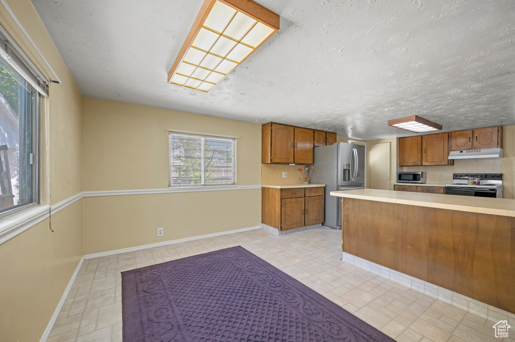 Kitchen featuring light countertops, appliances with stainless steel finishes, baseboards, and brown cabinetry