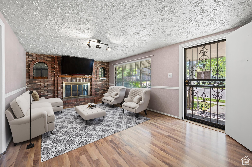 Living area with a textured ceiling, wood finished floors, baseboards, and a brick fireplace