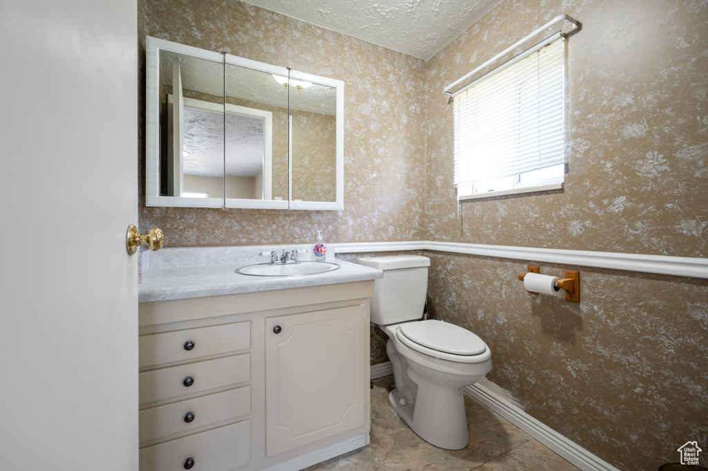Half bathroom with vanity, toilet, wallpapered walls, and a textured ceiling