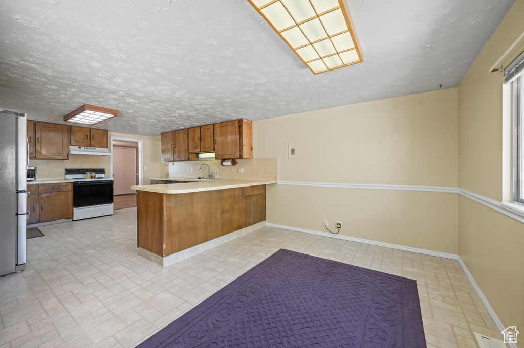 Kitchen with white electric range oven, a sink, freestanding refrigerator, a peninsula, and under cabinet range hood