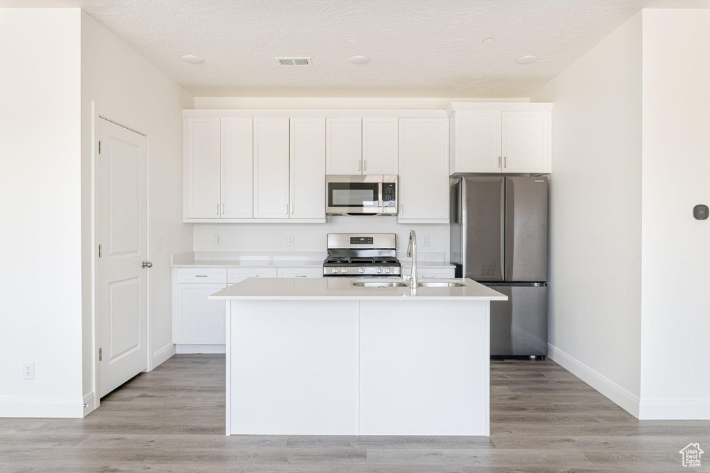 Kitchen with white cabinetry, baseboards, appliances with stainless steel finishes, and a kitchen island with sink