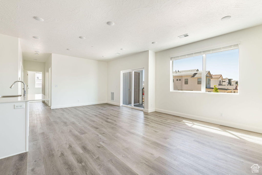 Unfurnished living room featuring baseboards, light wood-style flooring, visible vents, and a textured ceiling