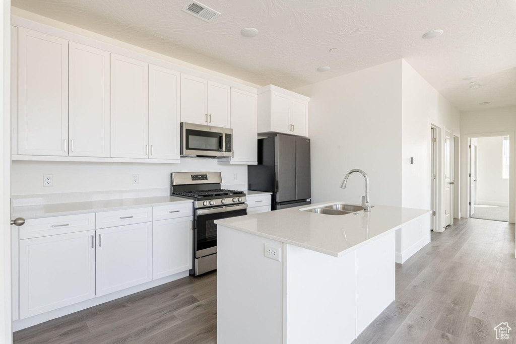 Kitchen featuring visible vents, a sink, light wood-type flooring, a kitchen island with sink, and appliances with stainless steel finishes