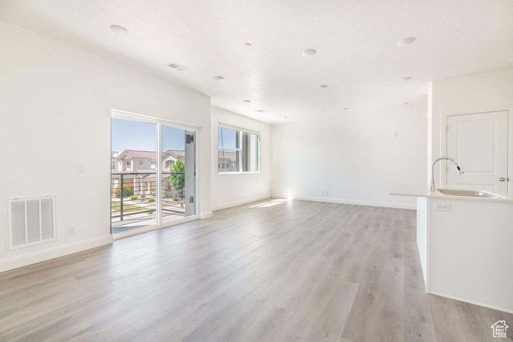 Unfurnished living room featuring visible vents, light wood finished floors, baseboards, and a sink