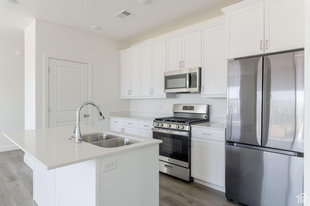 Kitchen featuring light wood finished floors, a sink, visible vents, an island with sink, and appliances with stainless steel finishes