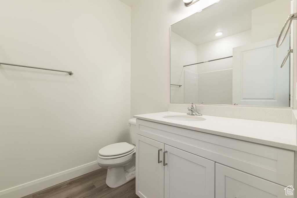 Bathroom featuring wood finished floors, vanity, a shower, baseboards, and toilet