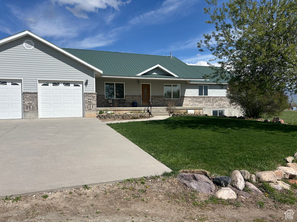 View of front of house with driveway, metal roof, a front yard, an attached garage, and a porch