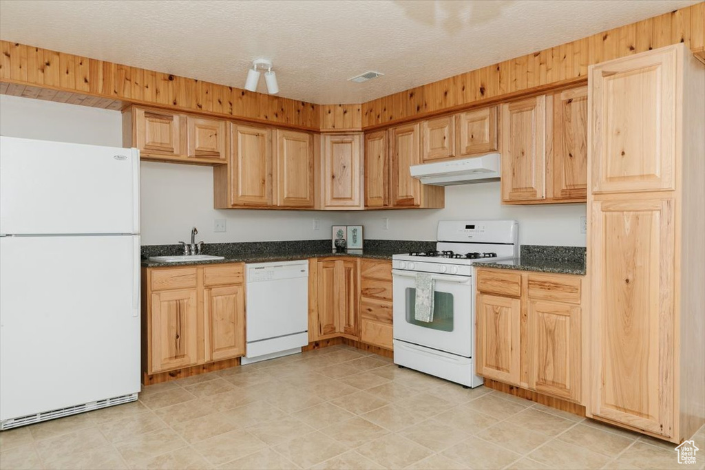 Kitchen with white appliances, under cabinet range hood, dark stone countertops, and light brown cabinetry