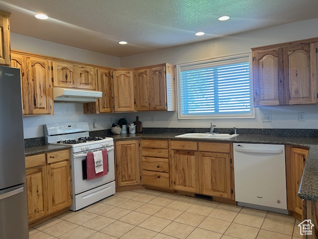 Kitchen with recessed lighting, a sink, under cabinet range hood, light tile patterned flooring, and white appliances