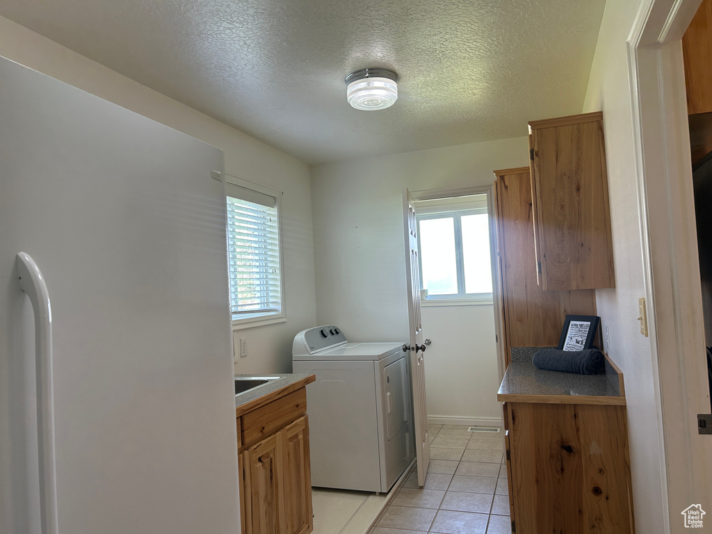 Laundry room with a textured ceiling, washer / clothes dryer, and light tile patterned flooring