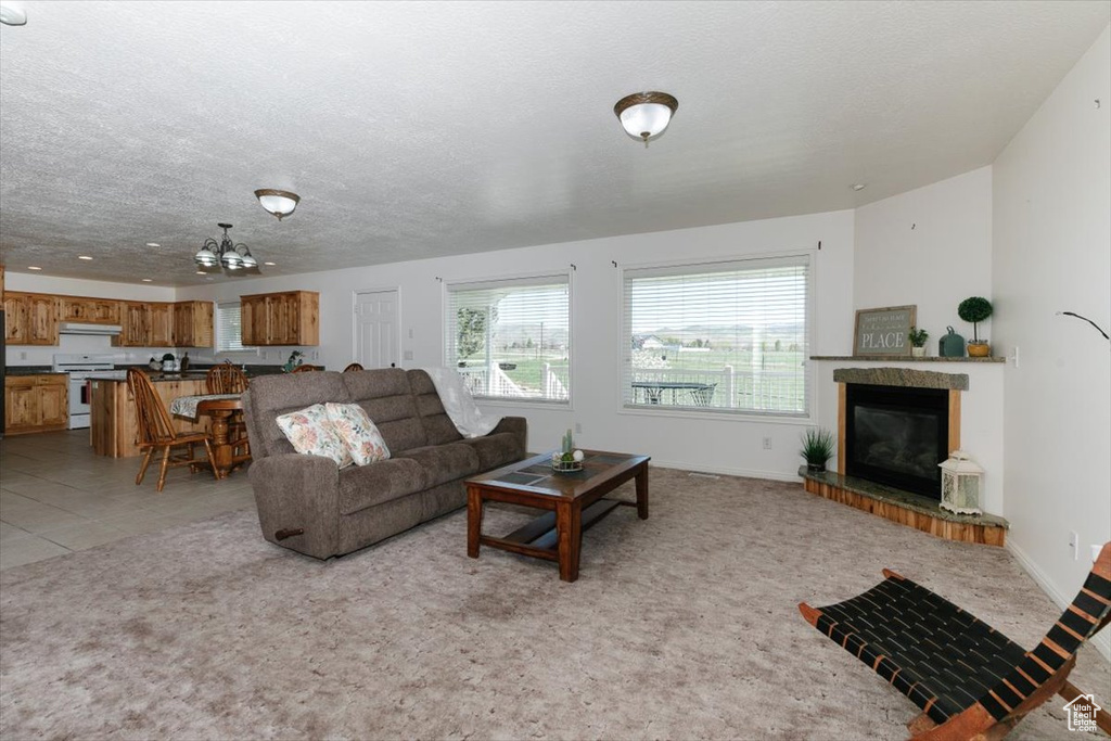 Living room featuring a tiled fireplace, a chandelier, a textured ceiling, and light carpet