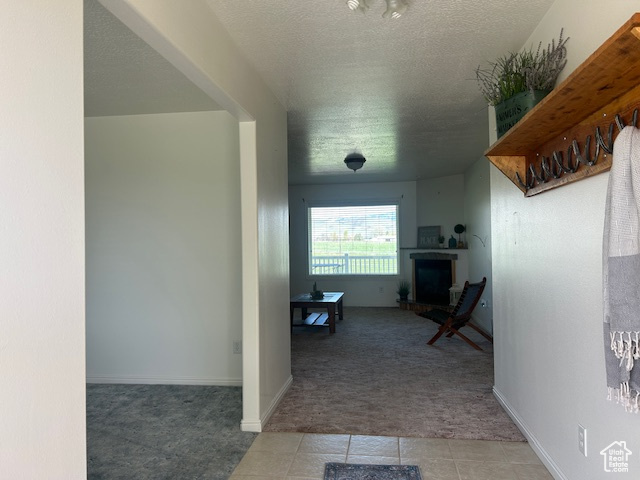 Corridor featuring tile patterned floors, baseboards, a textured ceiling, and carpet flooring
