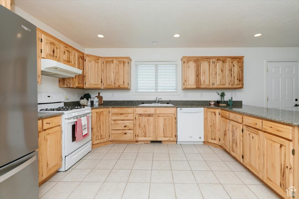 Kitchen featuring white appliances, under cabinet range hood, recessed lighting, dark stone countertops, and light brown cabinets