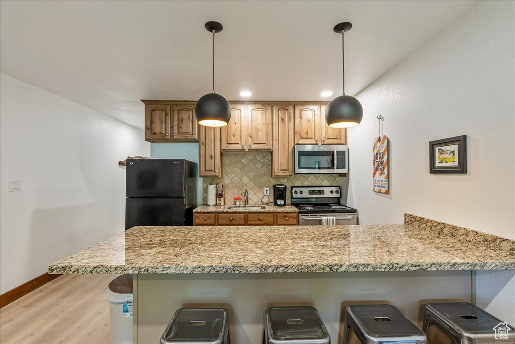 Kitchen with a peninsula, a kitchen breakfast bar, stainless steel appliances, and light wood finished floors