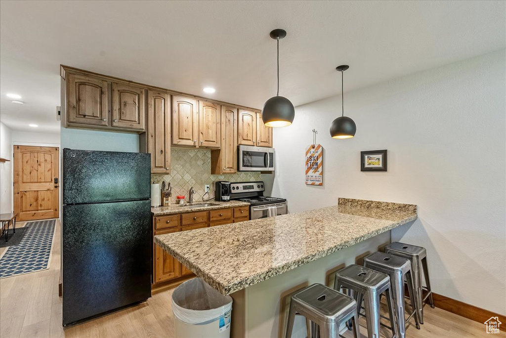 Kitchen featuring a breakfast bar, light wood finished floors, backsplash, a peninsula, and appliances with stainless steel finishes