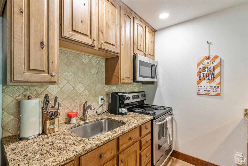 Kitchen with stainless steel appliances, a sink, light stone countertops, baseboards, and tasteful backsplash