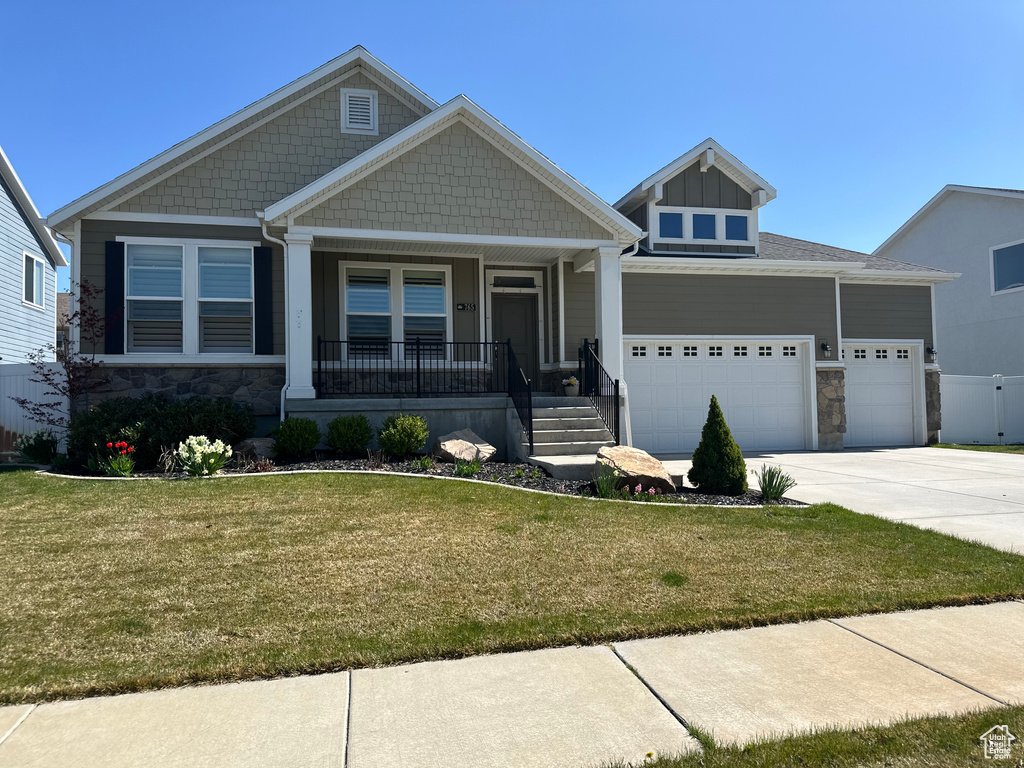Craftsman house featuring a garage, stone siding, a front lawn, and concrete driveway