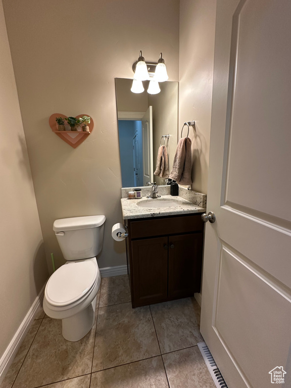 Half bath featuring tile patterned flooring, baseboards, toilet, and vanity