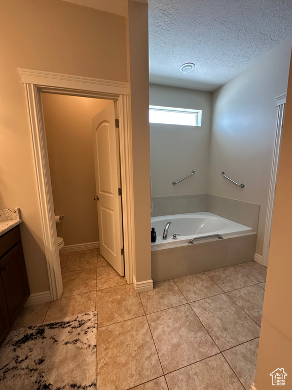 Bathroom with a bath, tile patterned floors, a textured ceiling, toilet, and vanity
