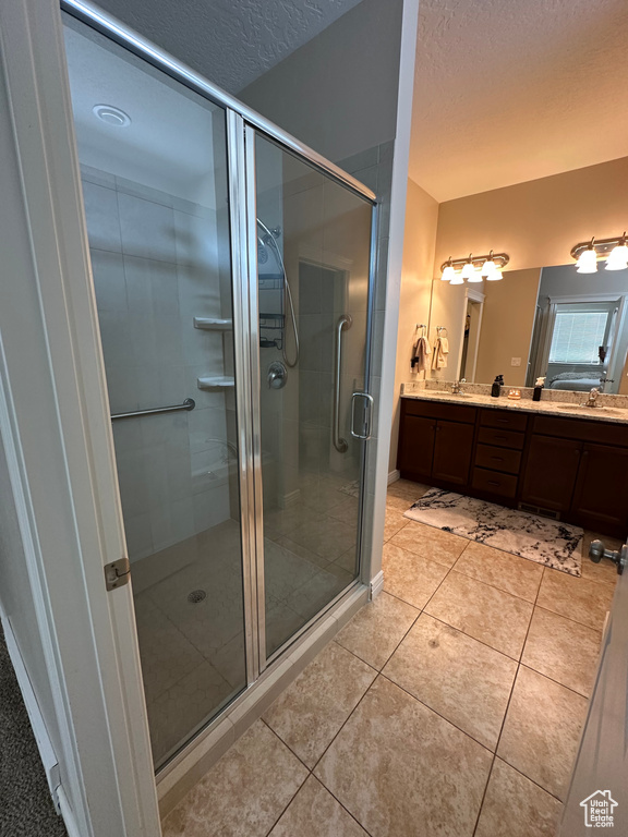 Bathroom featuring tile patterned flooring, double vanity, a sink, a textured ceiling, and a stall shower