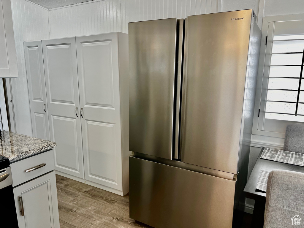 Kitchen with white cabinets, light wood-style flooring, light stone countertops, and freestanding refrigerator