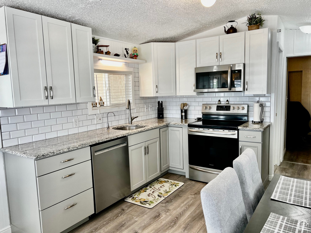 Kitchen with light wood finished floors, stainless steel appliances, a sink, and a textured ceiling