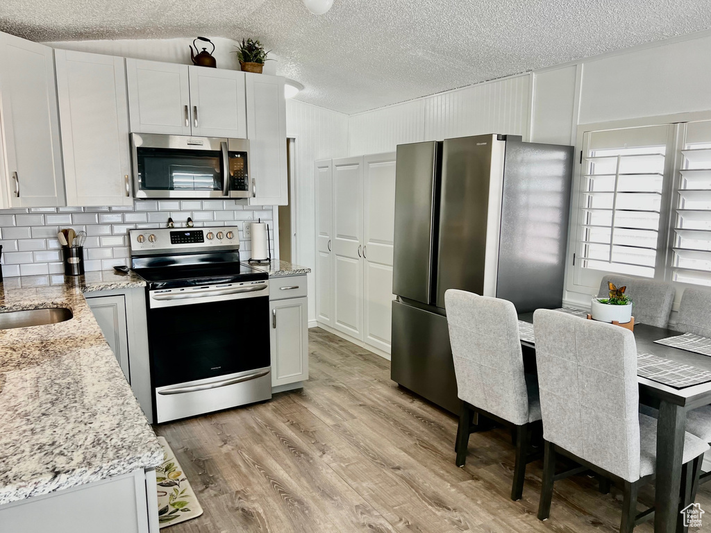 Kitchen with a textured ceiling, tasteful backsplash, light wood-style floors, light stone countertops, and appliances with stainless steel finishes